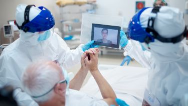 A patient in a hospital bed being assisted by staff to make a video call.