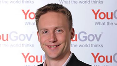 Politics graduate, Joe Twyman, pictured in front of a YouGov banner.