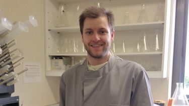 PhD Researcher - stands in lab and grey labcoat