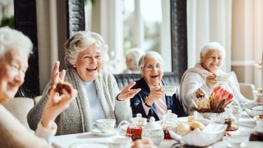 A group of older women sat talking round a table 