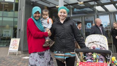Two female Partners English students, with one of them holding a child, stood in front of the University of Sheffield Students Union