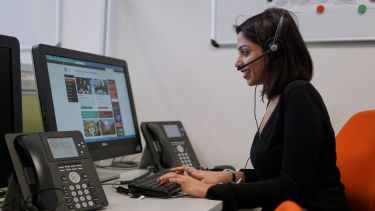 An image of a woman wearing a headset and microphone while sat next to a computer
