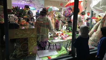 A community event with families interacting in a colourful shop, and children drawing on the windows to share their views on local architecture and developments