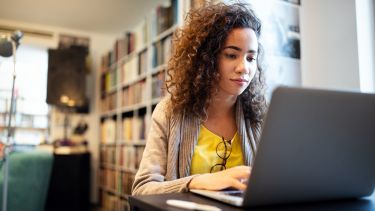 a young female student sat at a laptop working