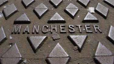 A photograph of the word 'Manchester' engraved onto a manhole cover.