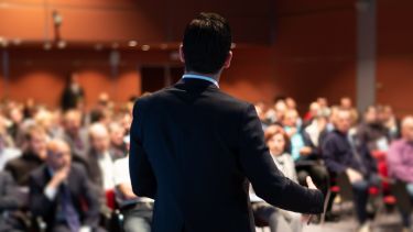 An image of a speaker presenting to a room full of people.