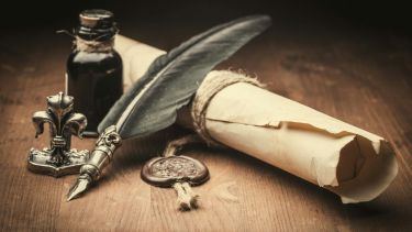 A photo of a quill and scroll next to a glass of ink