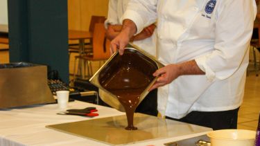 A man pouring melted chocolate from a metal tin onto a table