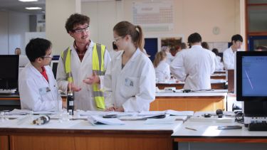 Three people wearing PPE in a lab, discussing an experiment