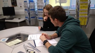 Two people sitting at a table looking at some work together