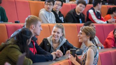 Students sat in a lecture theatre talking to a lecturer.