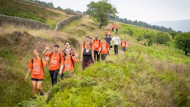 Group of Big Walk participants wearing orange t shirts and walking in a line through countryside