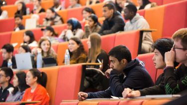 Students sat in a large lecture theatre with red and orange seats.