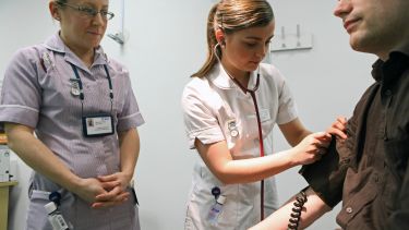 Student nurse examines a patient while another nurse watches