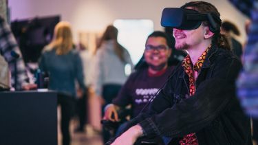 A smiling man sits in Millennium Gallery wearing a virtual reality headset