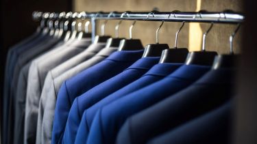 A collection of identical suit jackets in black, blue and grey on a hanging rack.