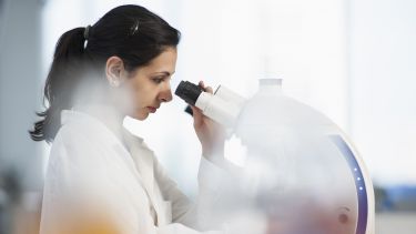 Woman in lab coat looking at a microscope