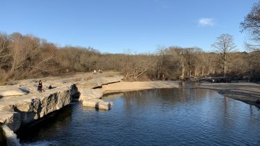 Image of McKinney Falls, America, a wide open lake with dry orange soil surrounding and a blue sky