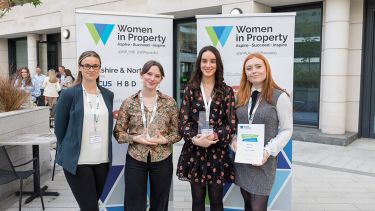 Four people, including our two students, standing in front of Women In Property banners. 