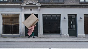 Woman walking up a street with a large box on back