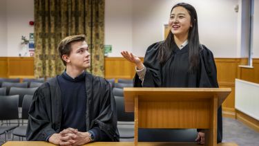 Two students stand in moot court in black robes