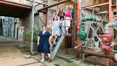 7 people standing on a metal stairs in what looks like a power station. Very Berlin vibe