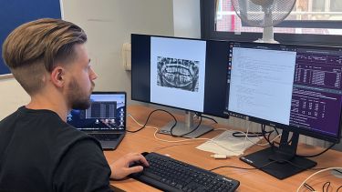 Insigneo summer research programme student working at a desk viewing computer code and dental images on computer monitors