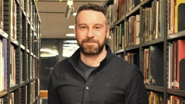 Alexis Thouki wearing a black shirt stood in a library.