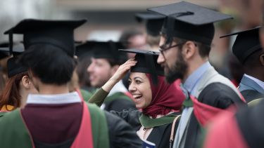 Postgraduate students smiling at graduation wearing caps and robes