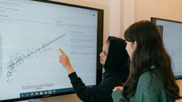 Two students look a graph on a large screen.