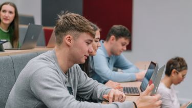 Luke Boaler sat in a lecture theatre wearing a grey jumper.