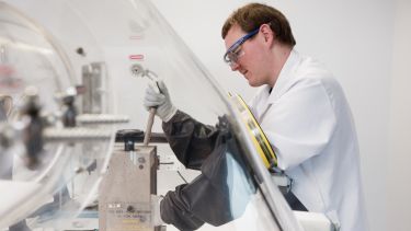 Side profile of a person wearing a lab coat and goggles and operating some machinery