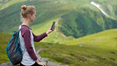 Photograph of a young woman sitting on a rock looking into her phone