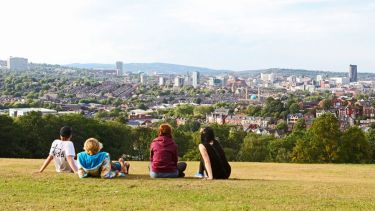 A scenic shot of some individuals sat on a green space overlooking the city