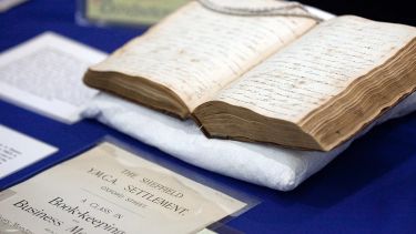 A close-up of a historical book open halfway through, with other historical documents near by
