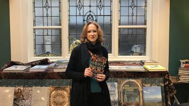 An image of Dr Caroline Dodds Pennock holding a copy of her new book 'On Savage Shores: How Indigenous Americans Discovered Europe'