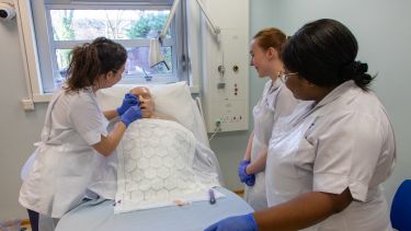 Three student nurses practicing on a dummy patient
