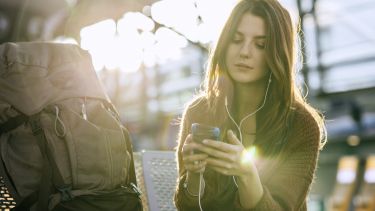 A woman sat on a bench using a mobile phone outside of an airport