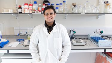 PhD student wearing white lab coat with lab equipment in background