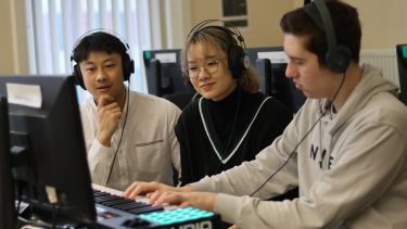 Three music students wearing headphones, working together with a keyboard and computer