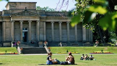 Groups of people relax on the grass in Weston Park under sunny blue skies