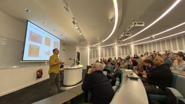 Photograph of Professor John Goodenough presenting his introductory lecture to a full house of staff from the Department of Electronic and Electrical Engineering