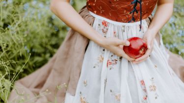 A Woman in White and Red Floral Dress Holding Red Apple Fruit.