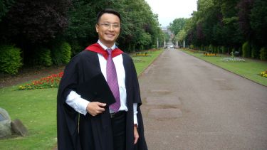 A graduating student wearing a graduation gown and holding his gap.