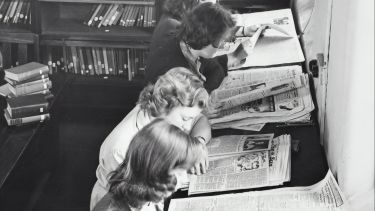 A line of women with 1950s hairstyles and clothing reading newspapers in a library.
