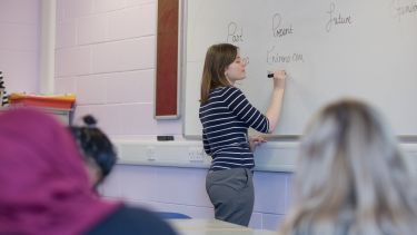Student teaching in a classroom and writing on a whiteboard