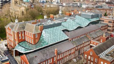 Aerial view of green glass atrium roof between two red brick buildings - both with lots of windows