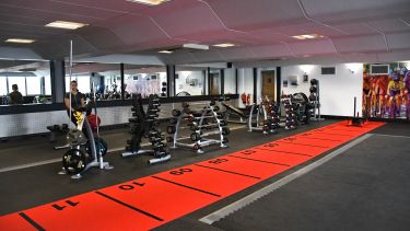 Gym area showing a red carpet strip with numbers 1 to 11 and racks with different hand held weights