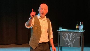 Actor in the French play with small moustache and waistcoat looks at the camera and lifts his finger warningly