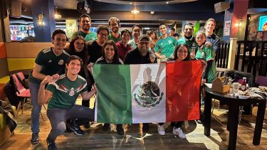 A group of people standing in a bar holding a Mexican flag